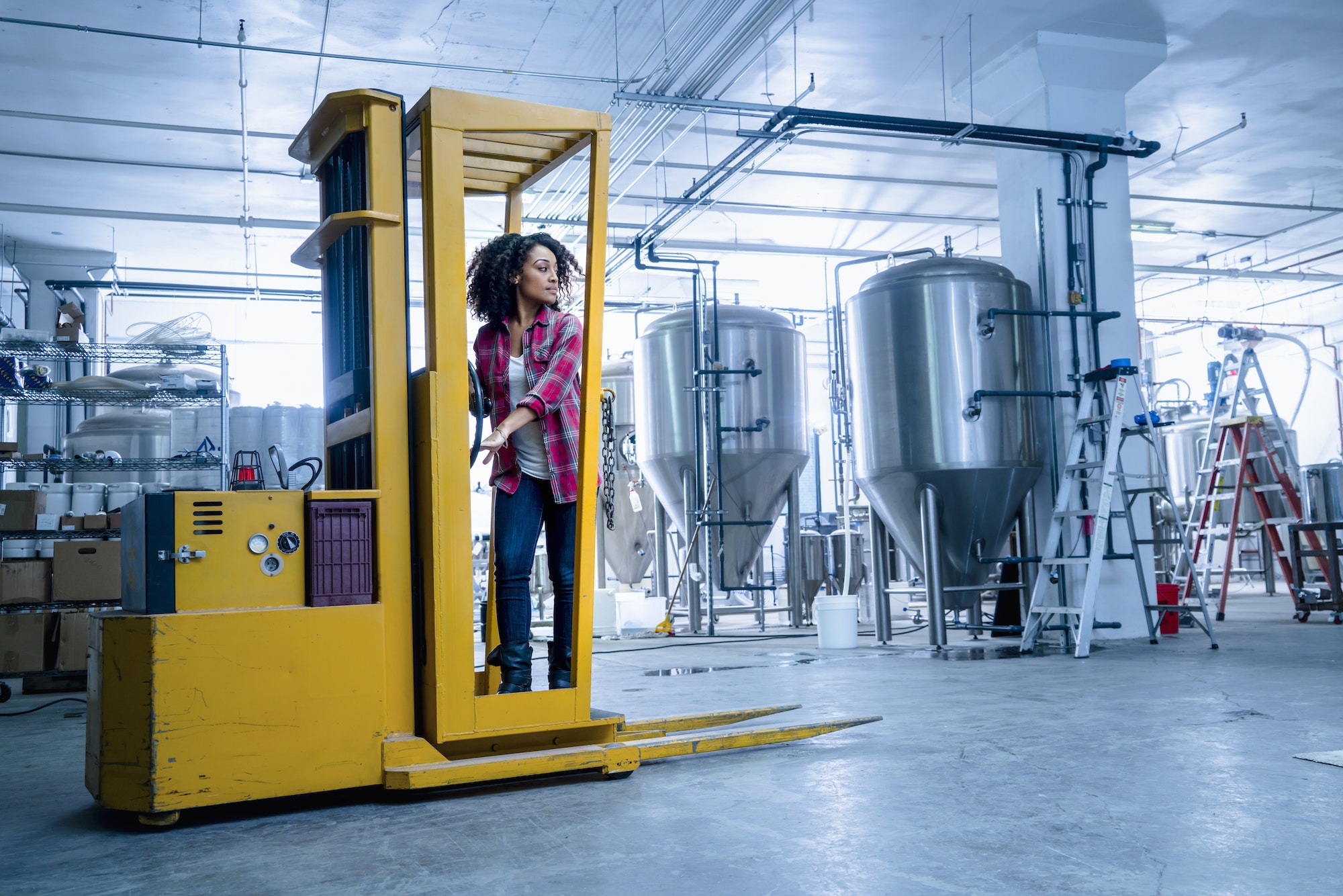 Mid adult woman in brewery driving forklift truck looking away